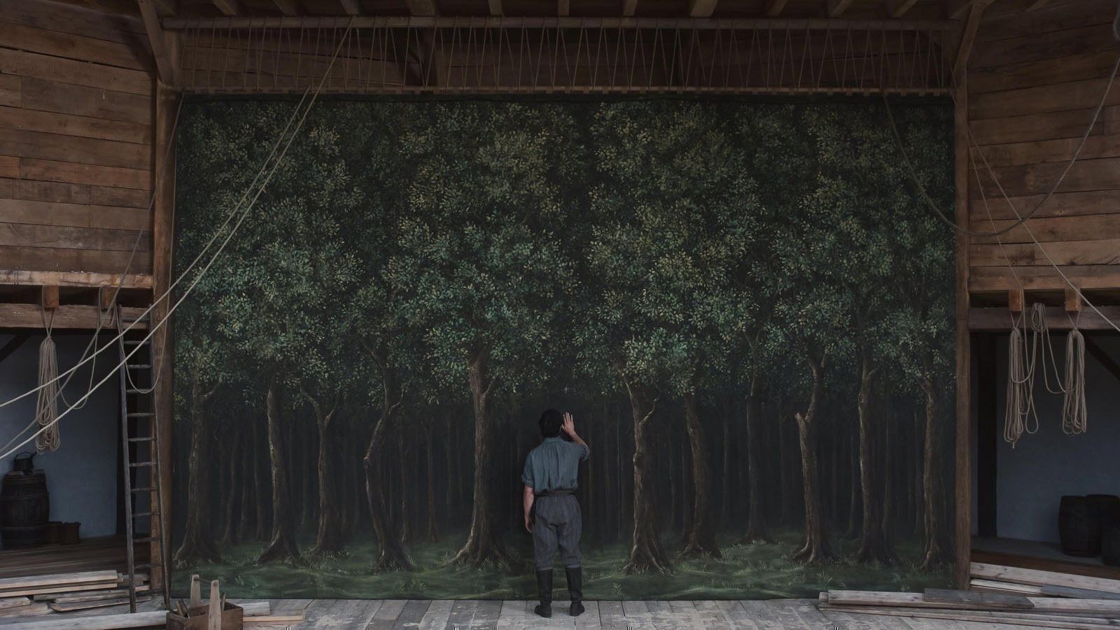 A figure standing before a painted forest backdrop on an open stage